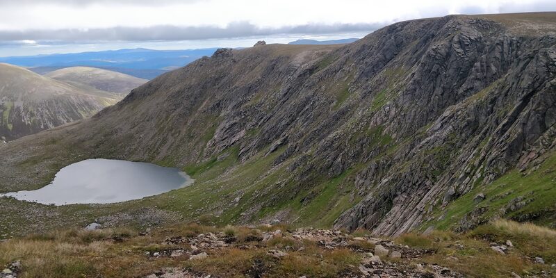 A lochan lying in a corrie below slabby cliffs.