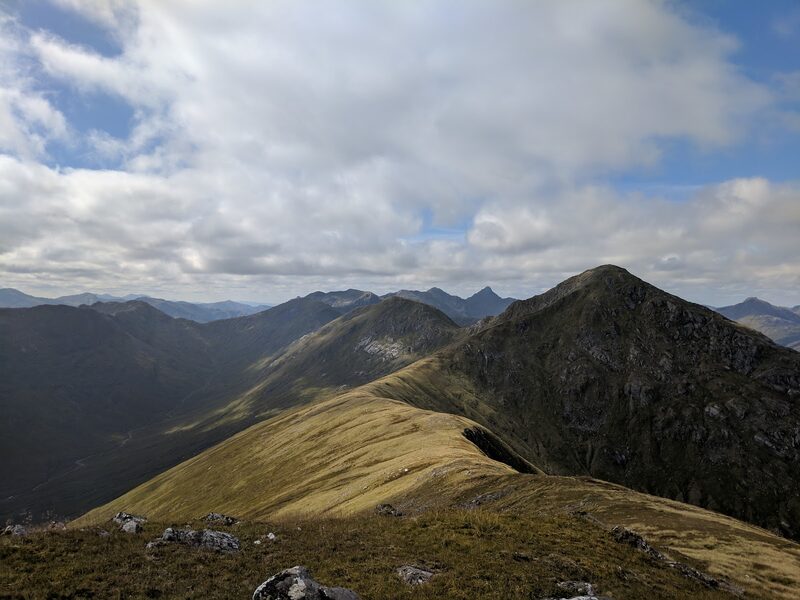 A grassy ridge leading to the dark, pointed top of Sgùrr Mòr, hills in haze beyond.