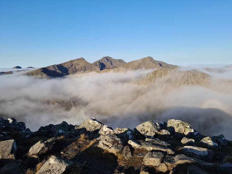 Summit rocks in low sun, with a line of peaks standing clear of the cloud.