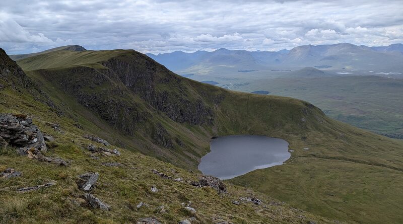 A dark lochan in the corrie of Beinn a' Chreachain, under a wall of crag, with a wide moor and far hills beyond.