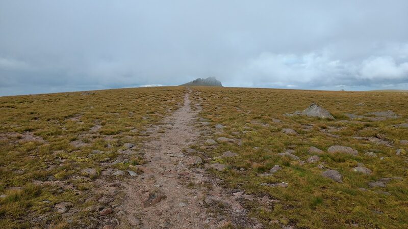 A path across the bare plateau towards a tor on the skyline, under low cloud.