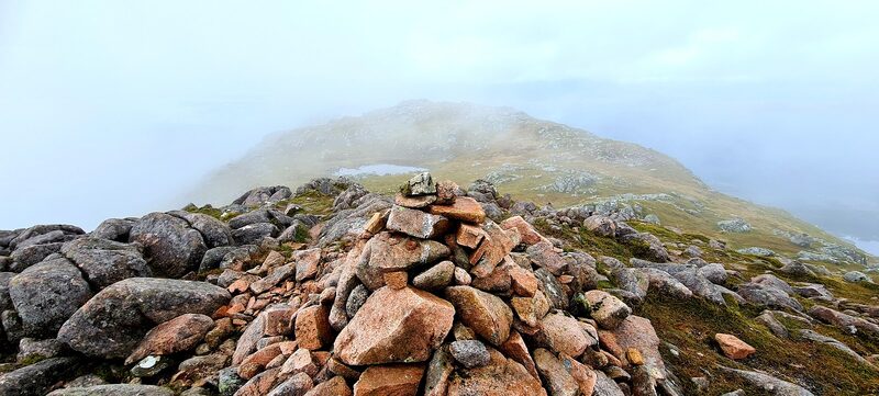 A cairn of red granite in mist, with another of the hill's tops showing through behind it.