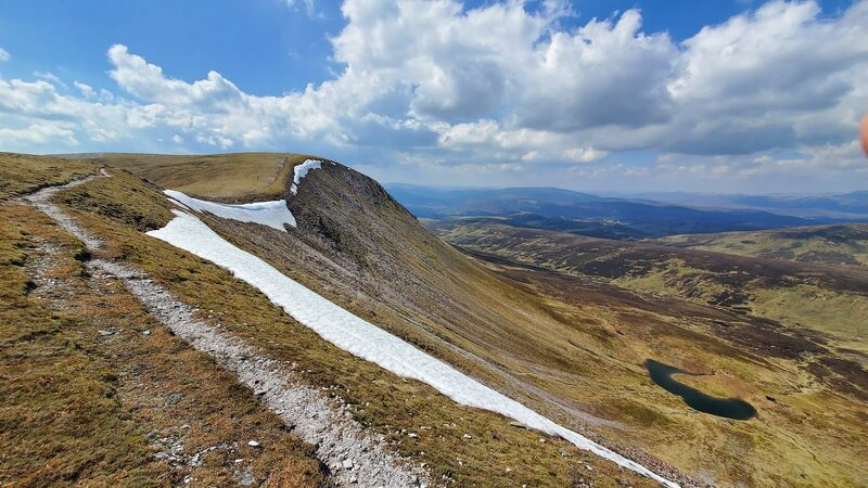 A ridge with a long snow patch on its steep side and a small loch below.