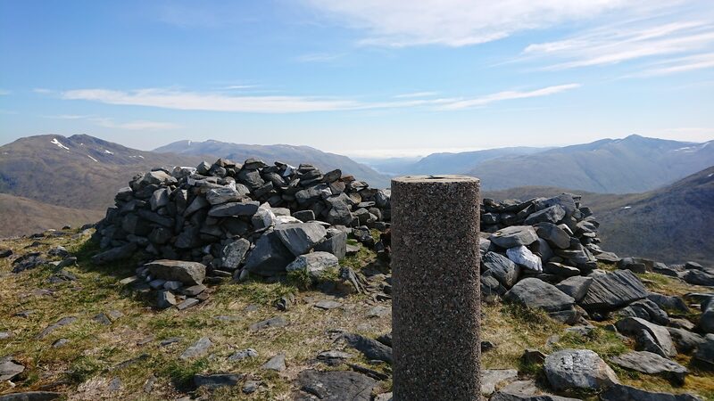 The round pillar on the summit of Beinn Fhada inside its low stone shelter, with hills beyond.