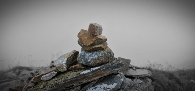 The summit cairn of Aonach air Chrith in mist, rust-coloured stones stacked on a long grey slab.