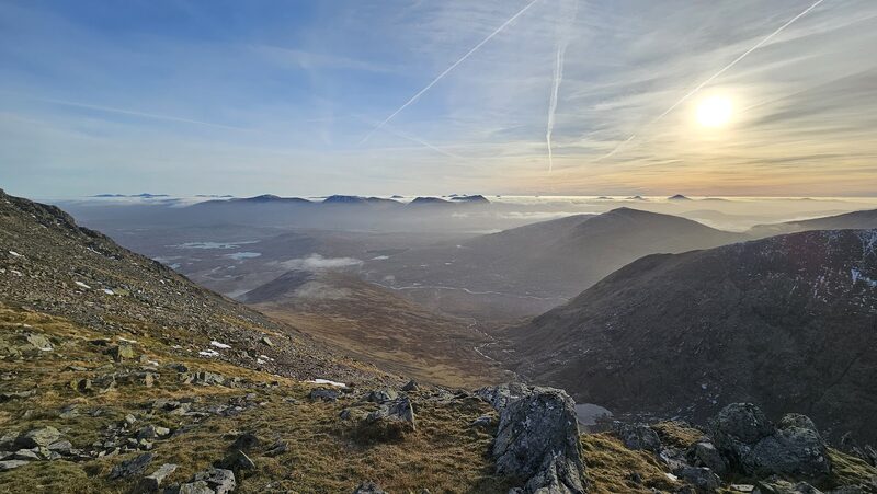 Low sun and vapour trails over the moor from a stony slope of the hill.