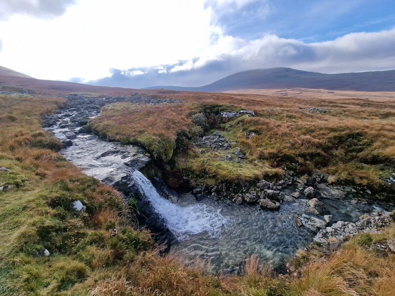 A burn falling over a rock step on the moor below Ben More, the hill behind under cloud.