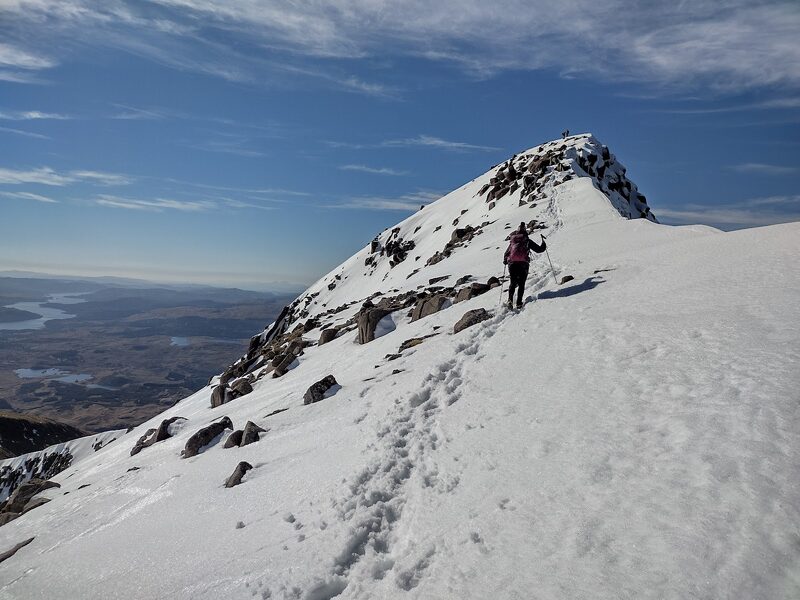 The last snow slope to the summit of Ben Cruachan in winter, one walker far ahead seen from behind, Loch Awe below.