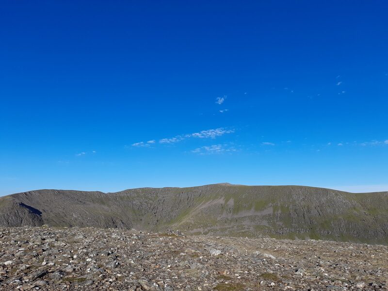 The hill's broad plateau and scooped east corries seen across the gap from stony ground under a deep blue sky.