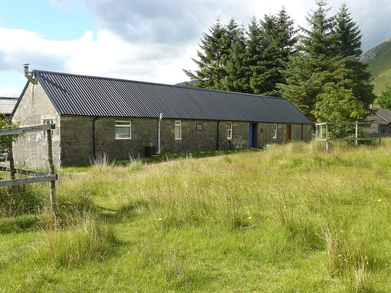 A long stone building with a dark tin roof at Barrisdale, with tall conifers behind.
