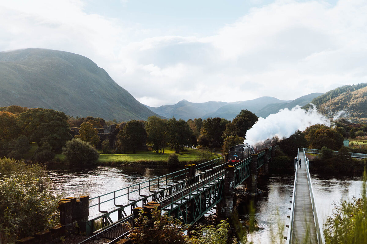 The Jacobite steaming along the West Highland Line beside a river among autumn trees.