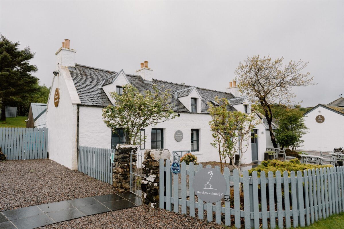 Whitewashed cottage with grey slate roof behind a pale blue picket fence