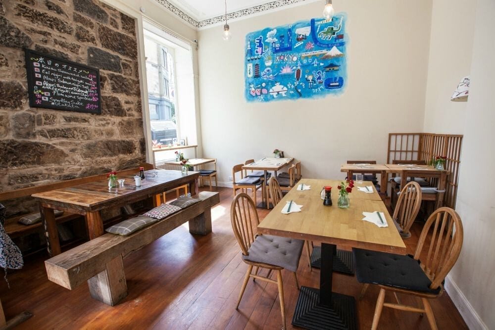 Wooden tables and benches beneath a blue artwork on a stone wall
