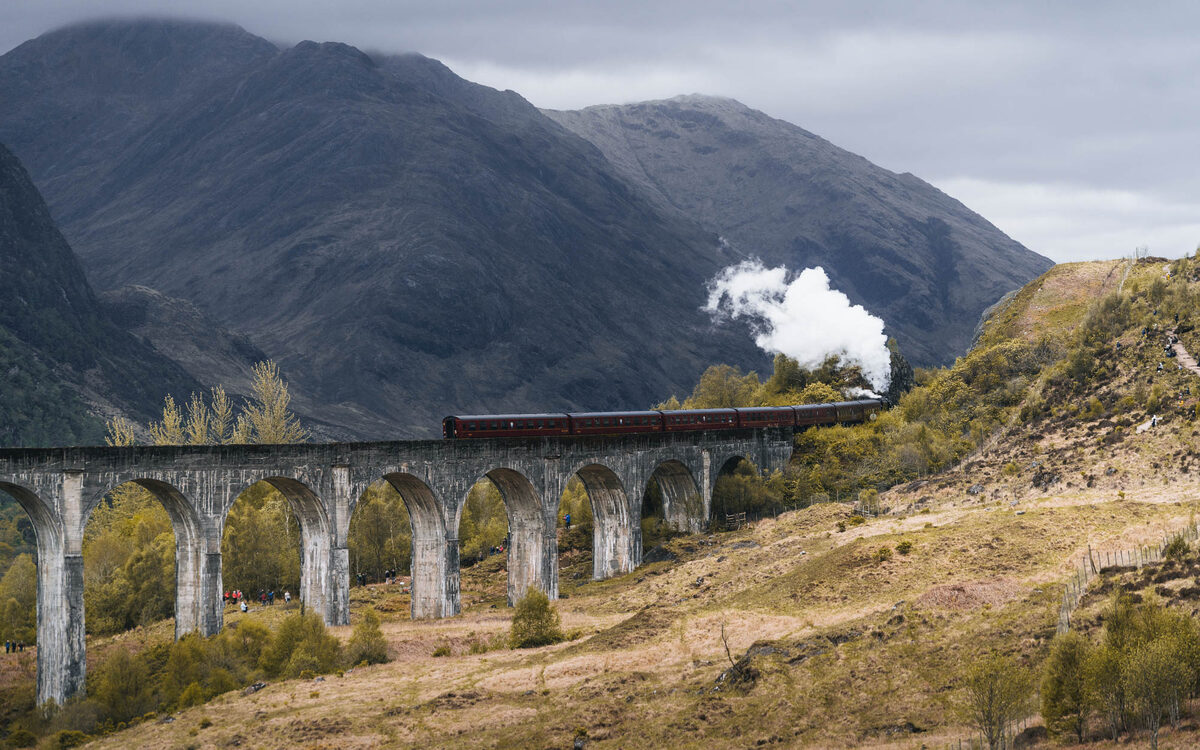 The Jacobite steaming across the curve of the Glenfinnan Viaduct, the hills behind.