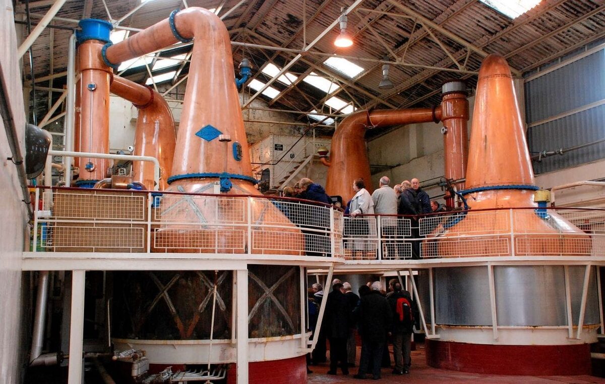 The copper stills in the still house at Ben Nevis Distillery, a group of visitors among them.