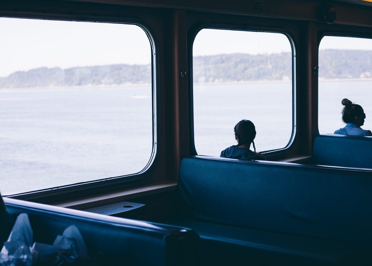 Passengers seated by ferry windows overlooking calm water and distant hills