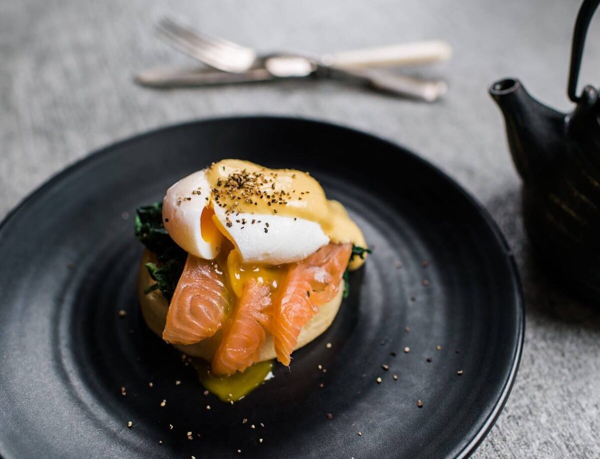 Poached egg and smoked salmon on a black plate with black teapot