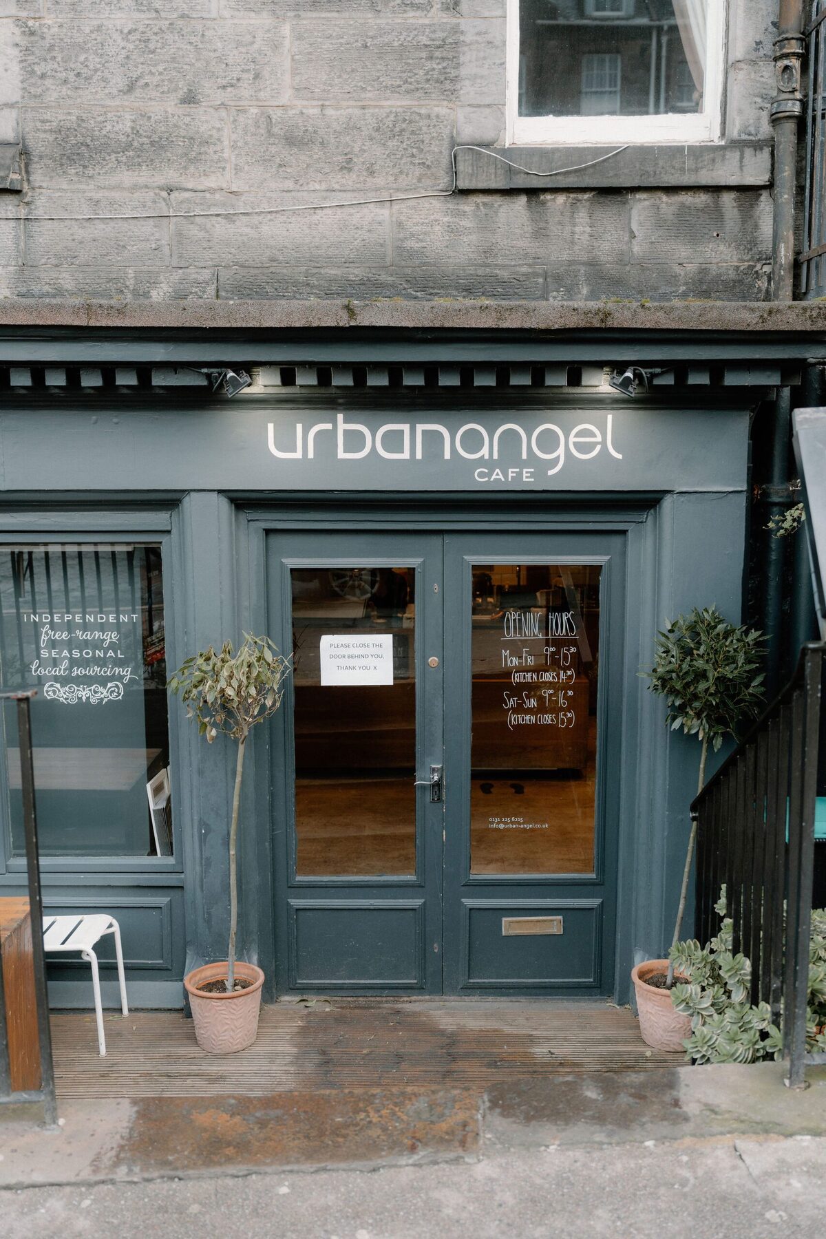 Urban Angel Cafe frontage in dark teal, with potted bay trees either side