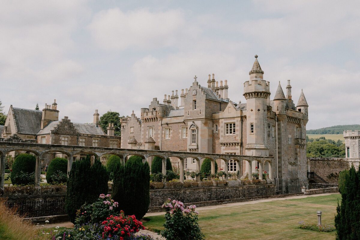 Turreted mansion with gardens, hedges and rose beds below a covered walkway