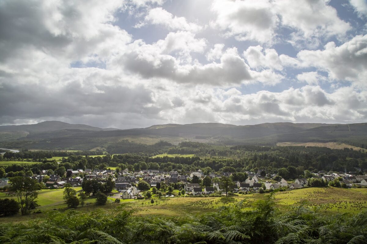 Village nestled among green fields and hills under a cloudy sky