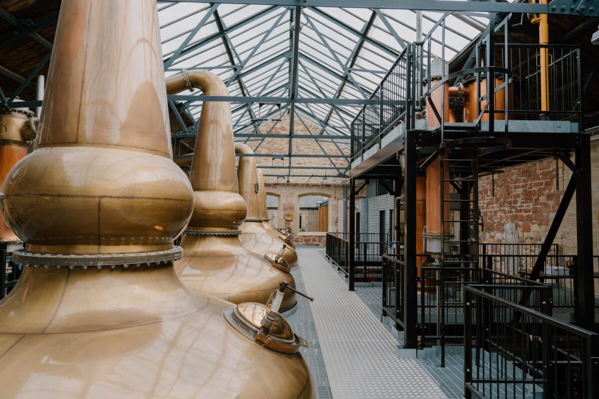 Copper stills lined up beneath a glass roof in a distillery