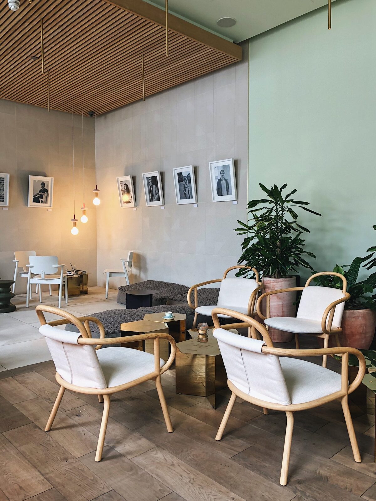 Rattan armchairs and brass tables under framed portraits in a lounge area