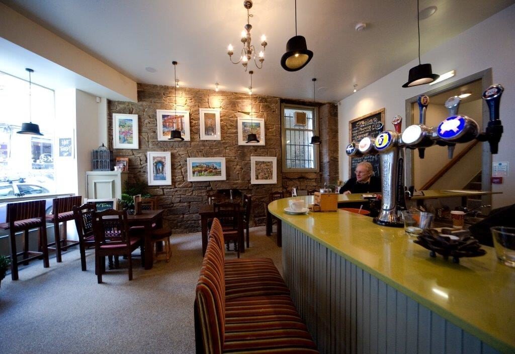 Framed pictures line an exposed brick wall beside a yellow-topped bar with beer taps