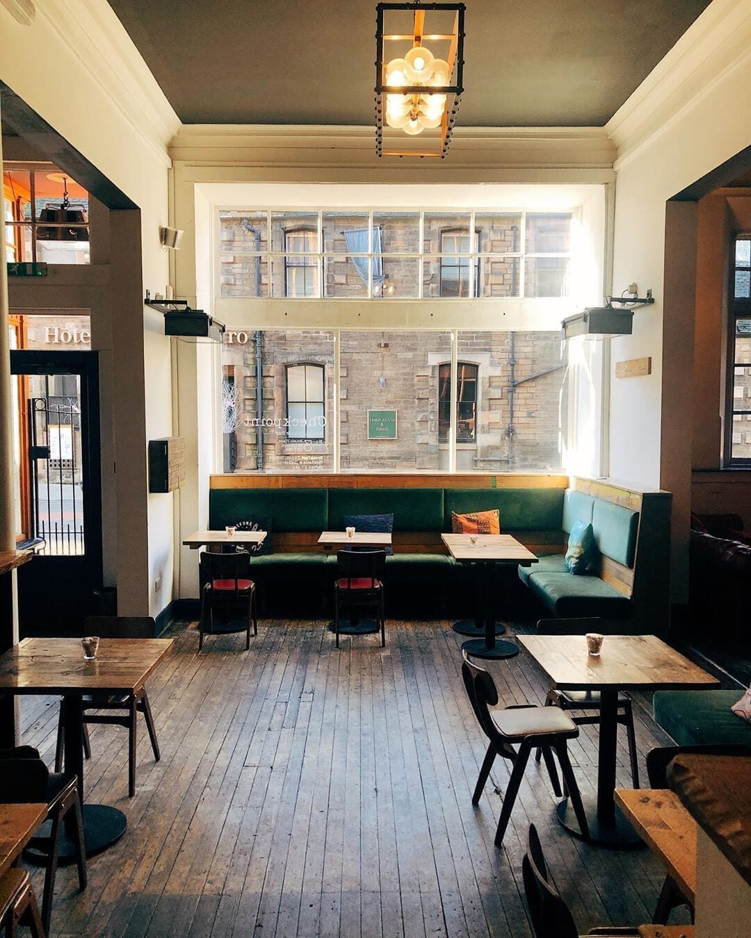 Green banquette seating and wooden tables inside a bar with large sash windows