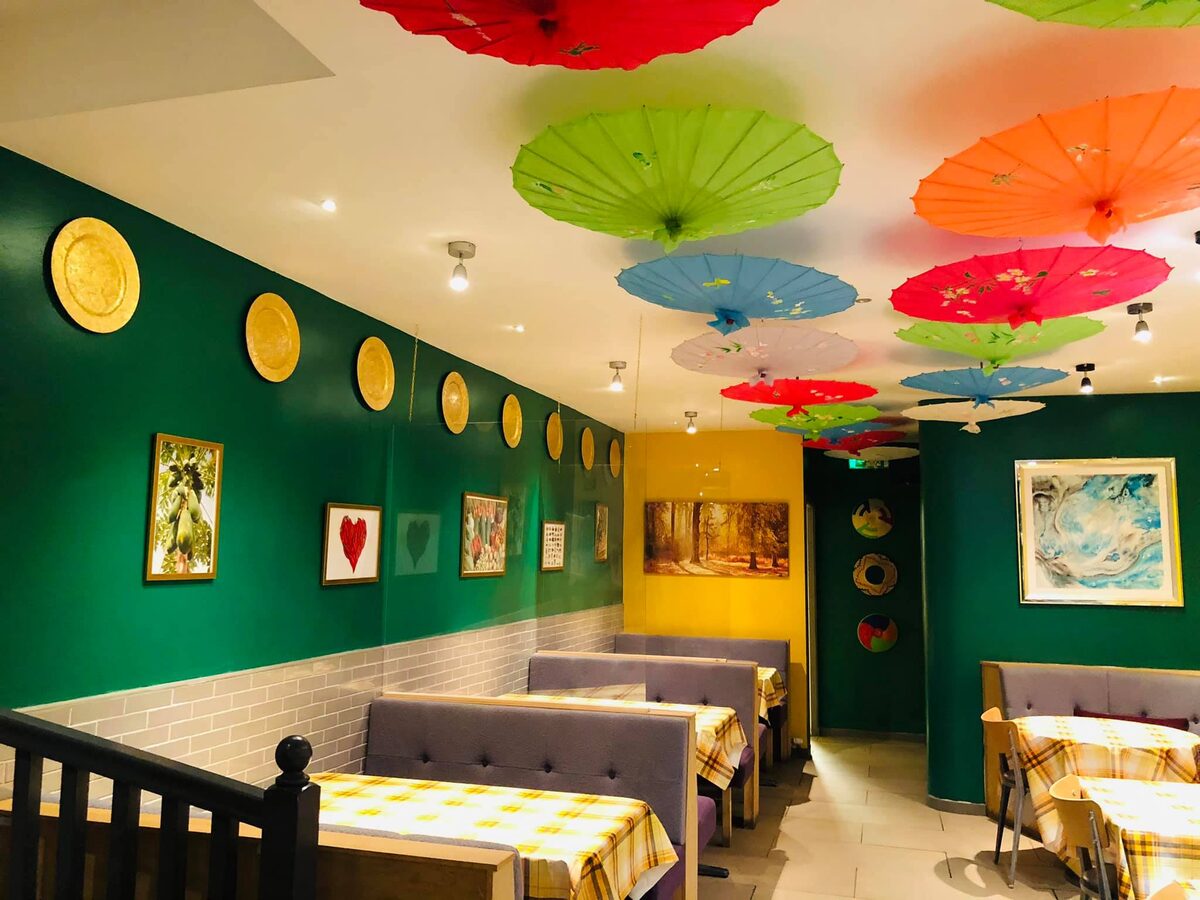 Coloured parasols hang above a green-walled restaurant with gold plates and framed artwork