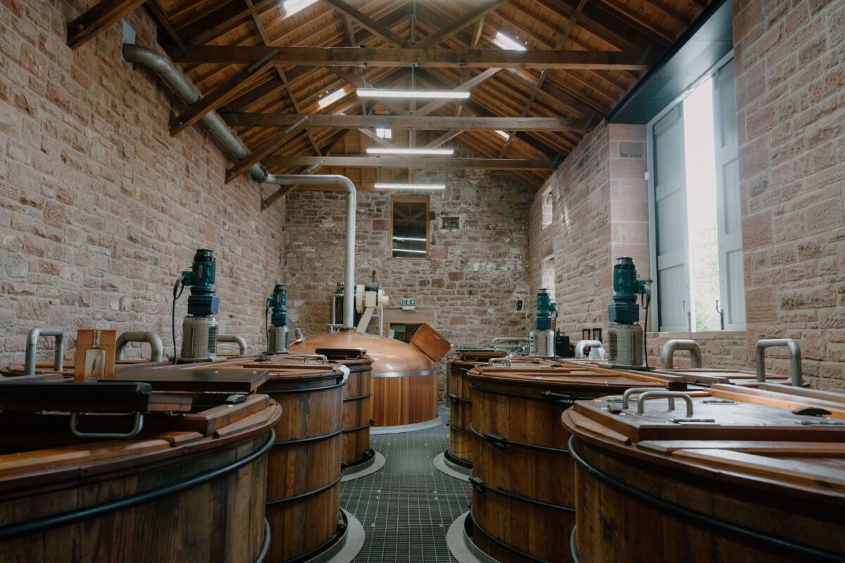 Wooden washbacks line a distillery hall with exposed brick walls and timber roof beams
