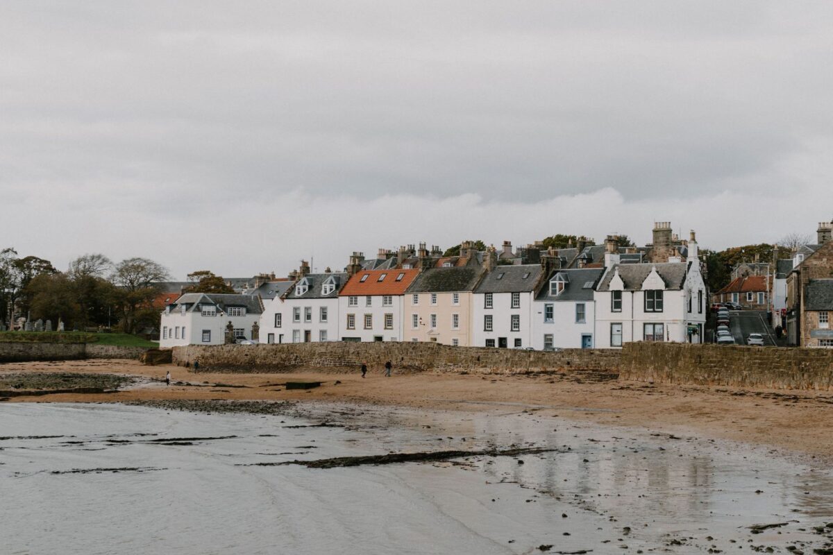 Row of white and grey houses along a sandy shoreline under grey skies
