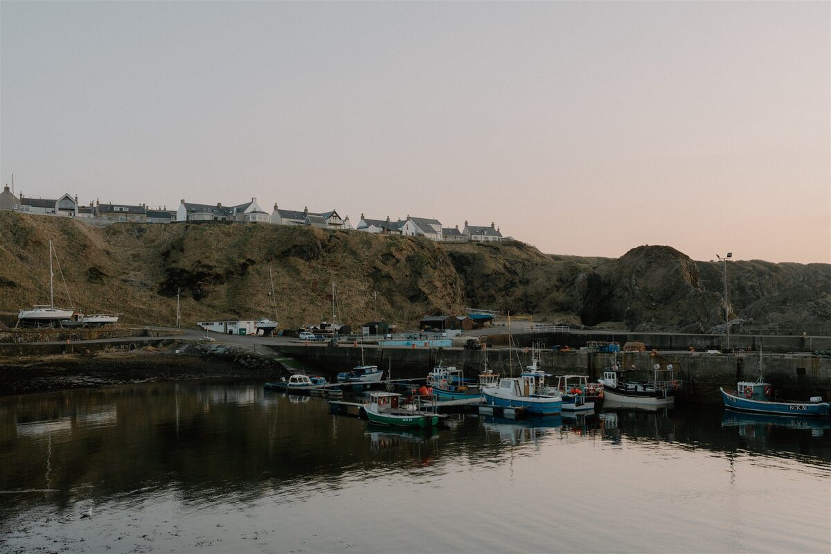 Fishing boats moored in harbour below whitewashed cottages on a grassy hillside