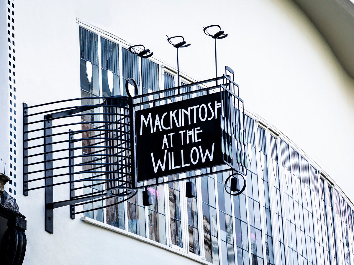 The Mackintosh at the Willow sign in black ironwork against the white front of the tearooms.