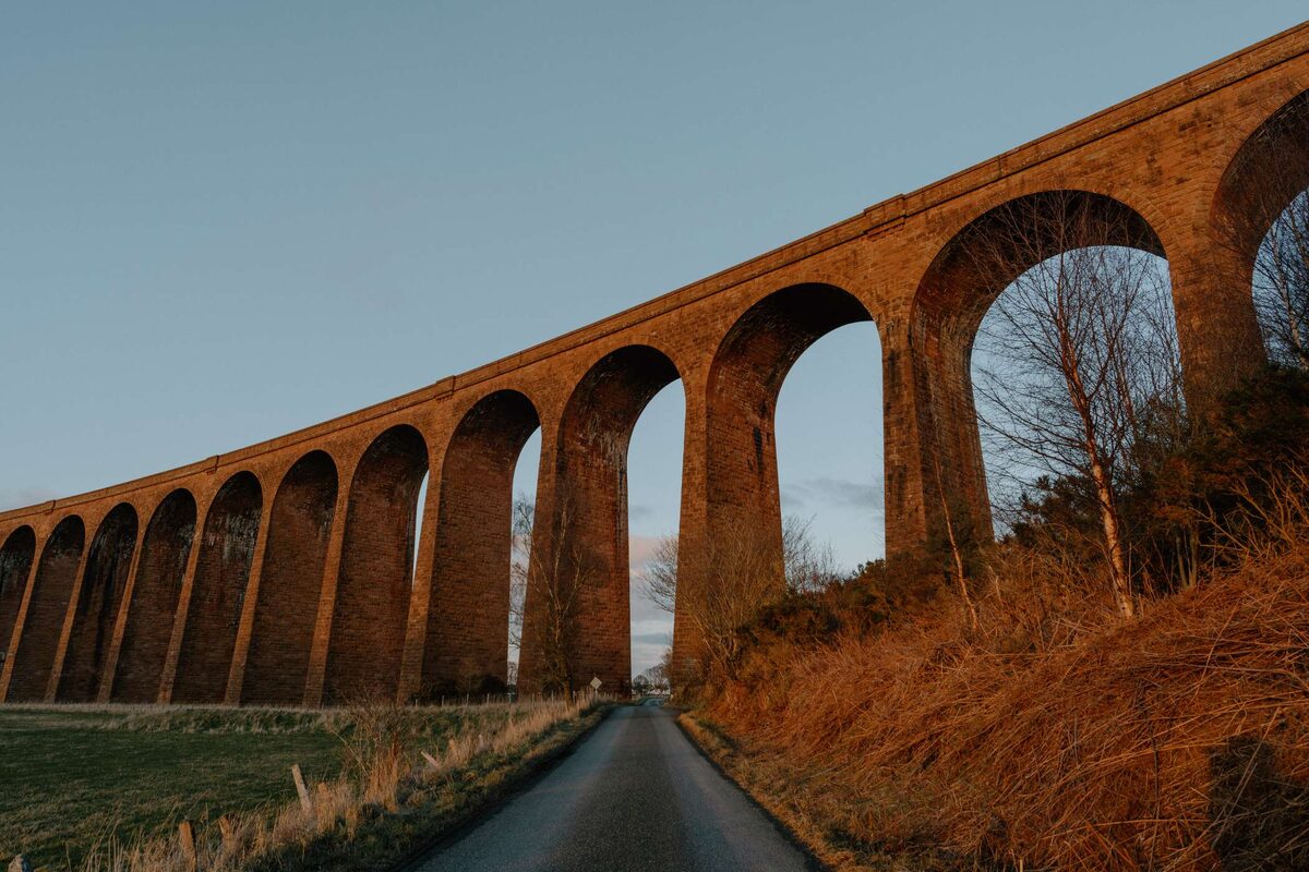 Brick railway viaduct arches stretching over a country road at dusk