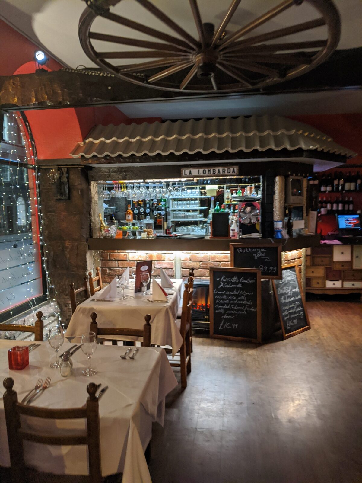 Cart wheel hangs above the "La Lombarda" bar, with laid tables and chalkboard menus
