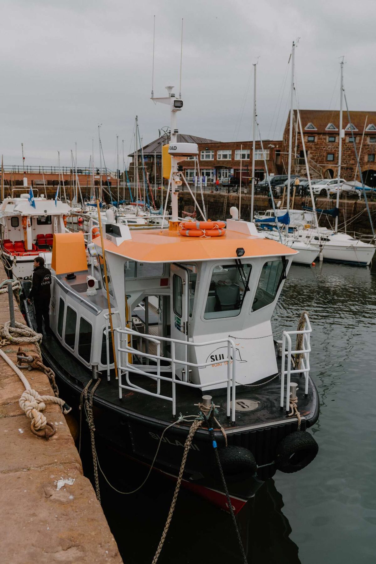 Orange-roofed harbour boat moored beside sandstone buildings and yacht masts