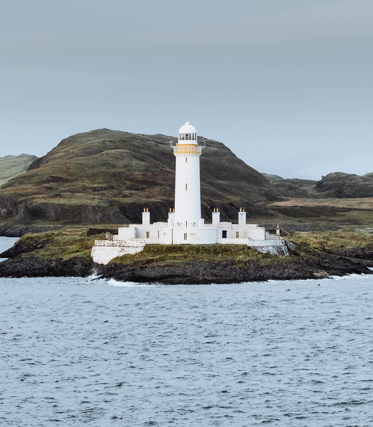 The white lighthouse and its buildings on the rocky islet.