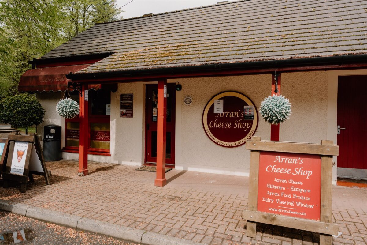 Arran's Cheese Shop entrance with red pillars and a wooden signboard outside