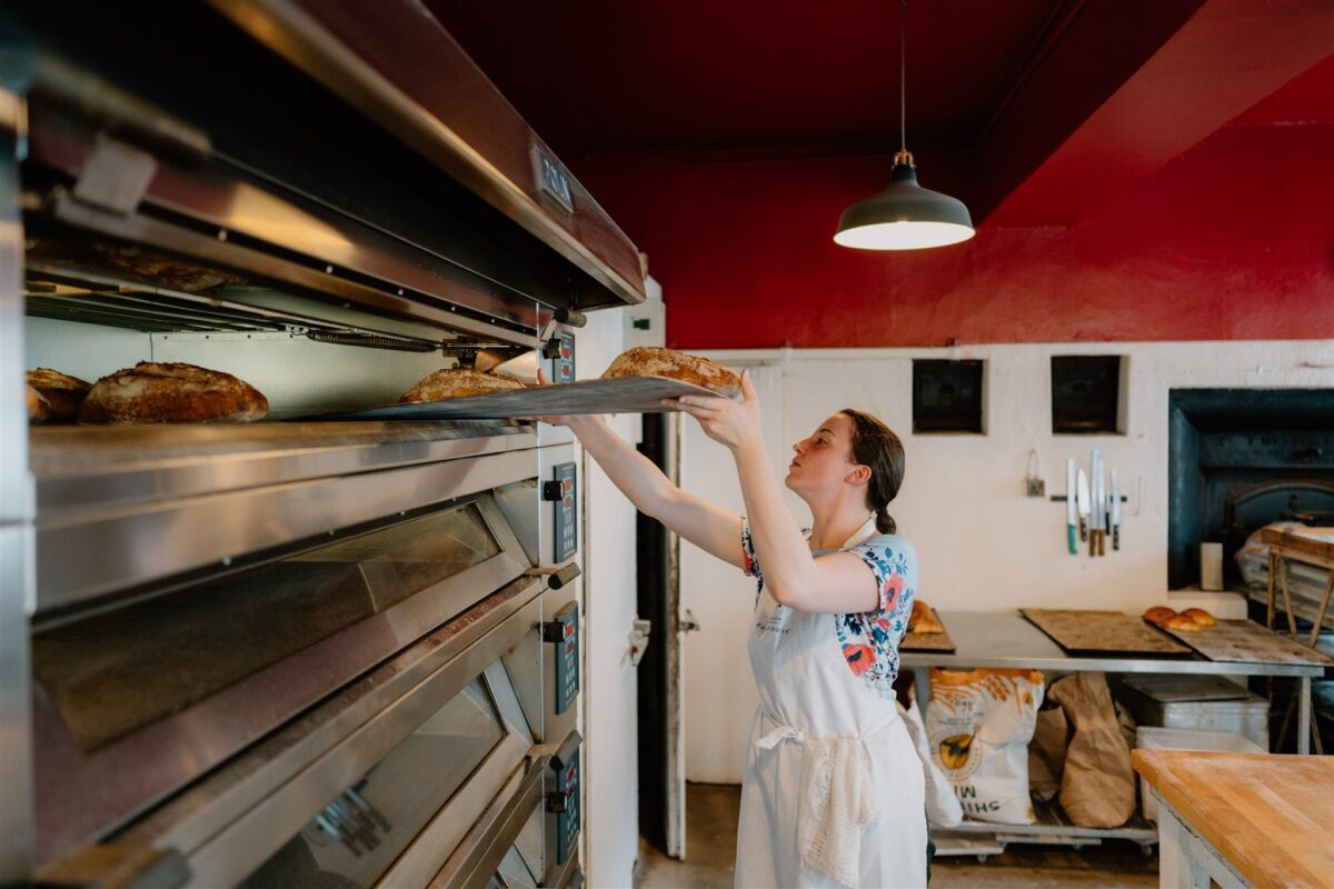 Baker lifts a fresh loaf from the oven in a red-walled bakery