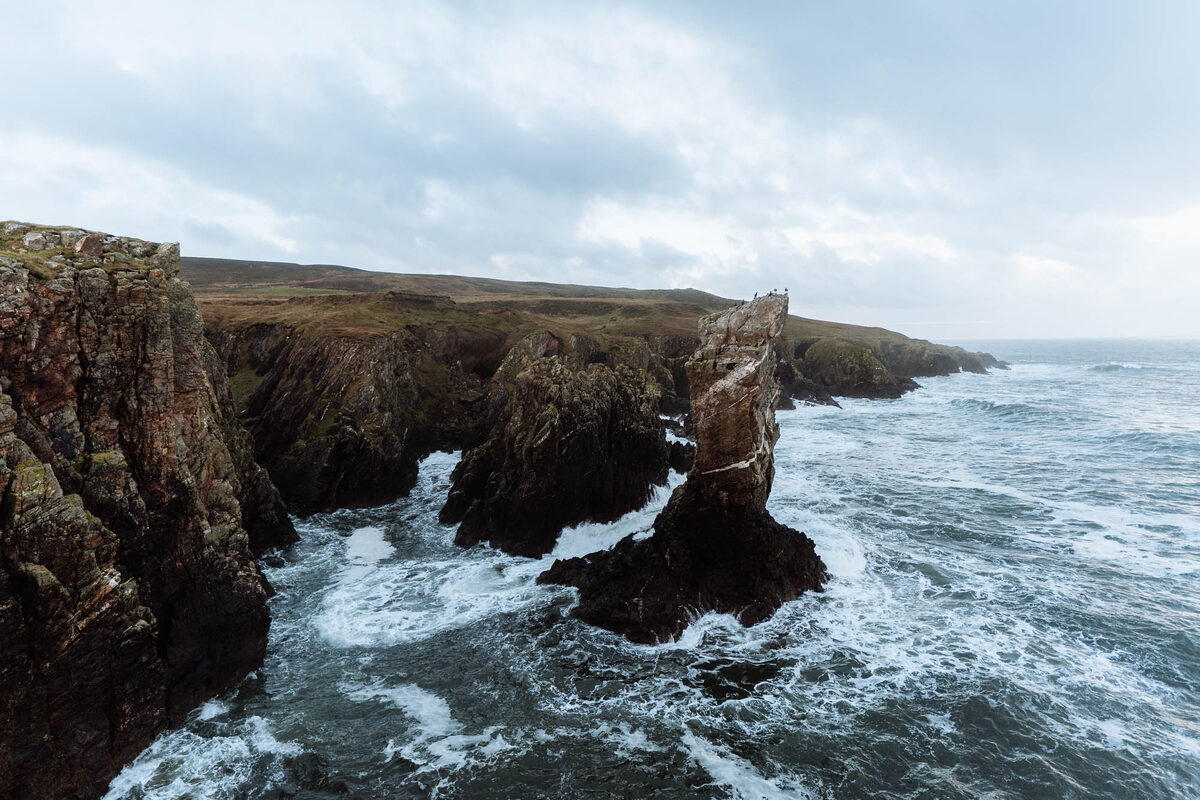 Soldier's Rock rising from white surf below the dark cliffs of the Oa.