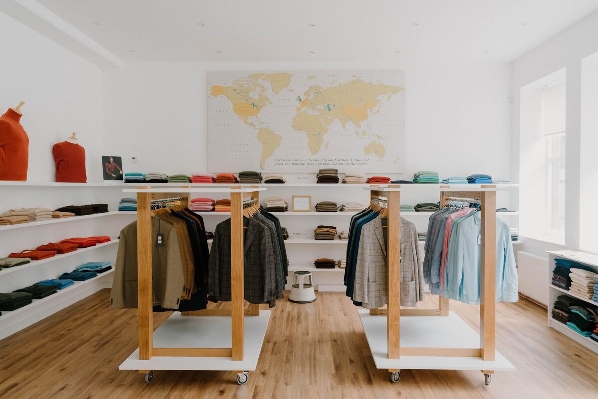 Clothing shop interior with wooden rails, folded jumpers on shelves and a world map