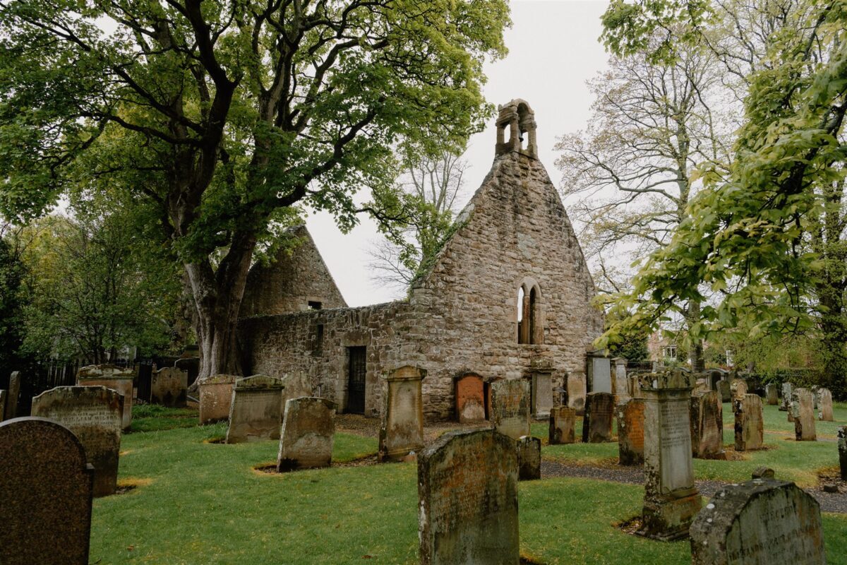 Ruined stone church with bellcote surrounded by weathered gravestones among trees