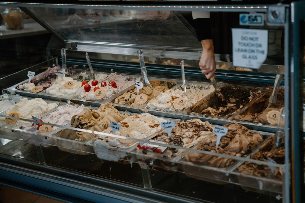 Gelato display case with a "do not touch or lean on glass" sign