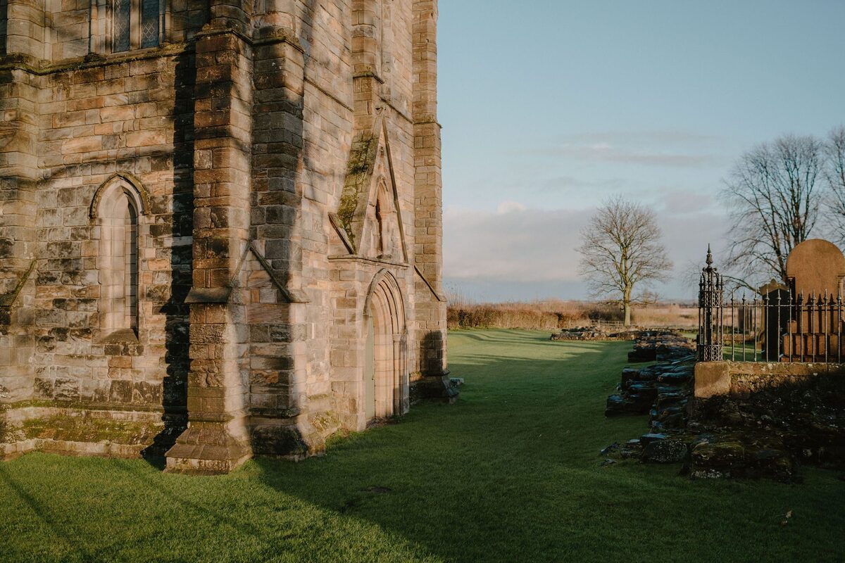 Stone abbey tower beside a graveyard with wrought-iron railings and gravestones