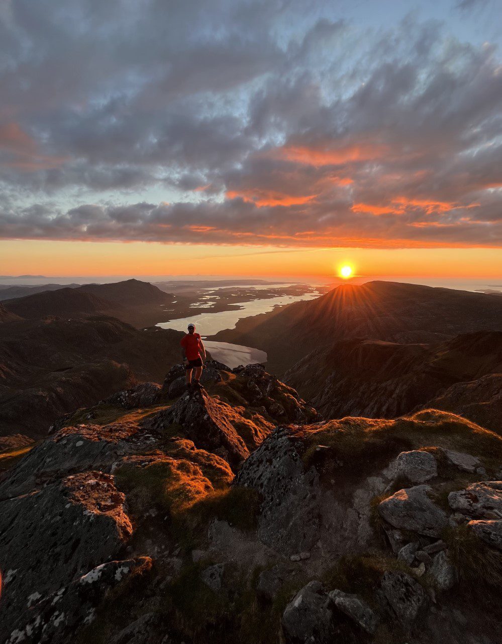 Hiker in red watches the sun set over a mountain ridge