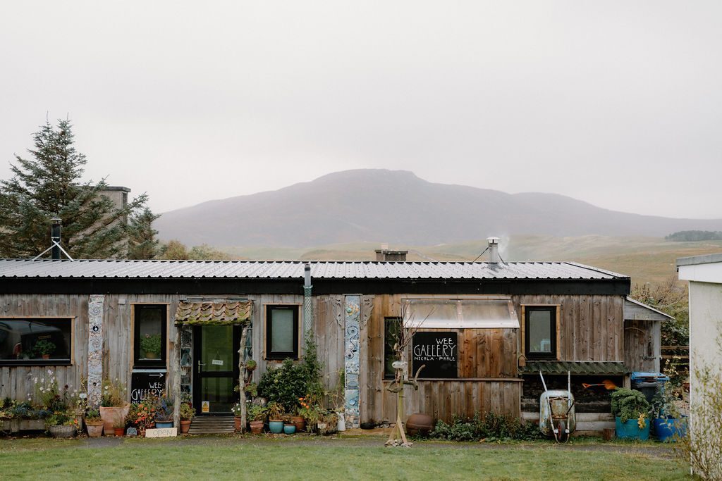 Wooden gallery building with potted plants and a hill behind