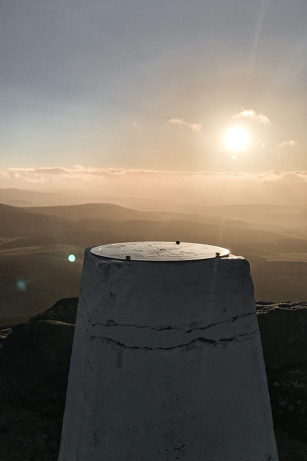 Concrete trig point overlooking layered hills at sunset