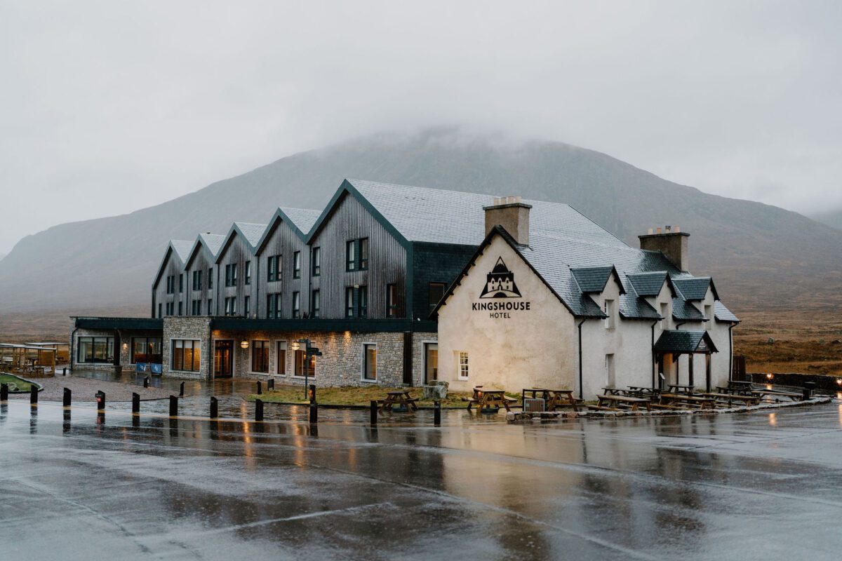Kingshouse Hotel beneath cloud-covered mountains, rain pooling on the car park