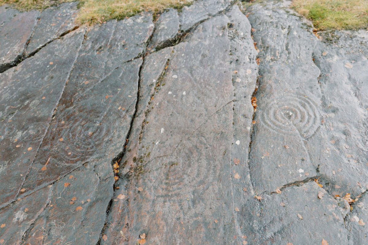 Cup and ring carvings etched into weathered rock, cracks running across the surface