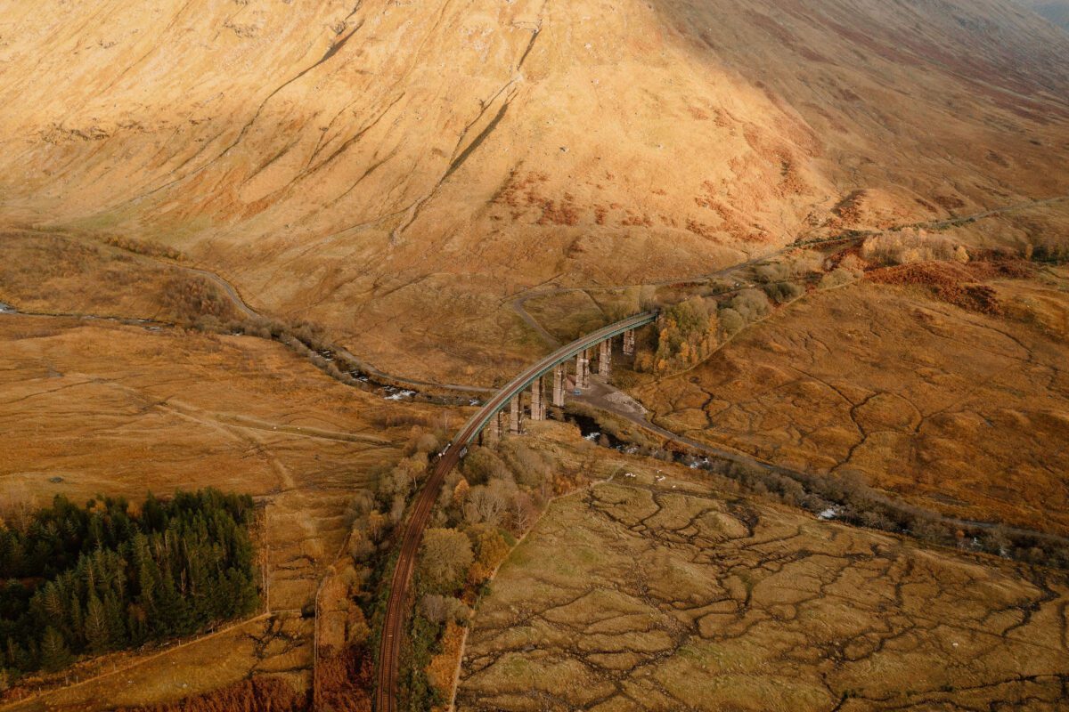 Curved railway viaduct crossing moorland below a steep russet mountainside